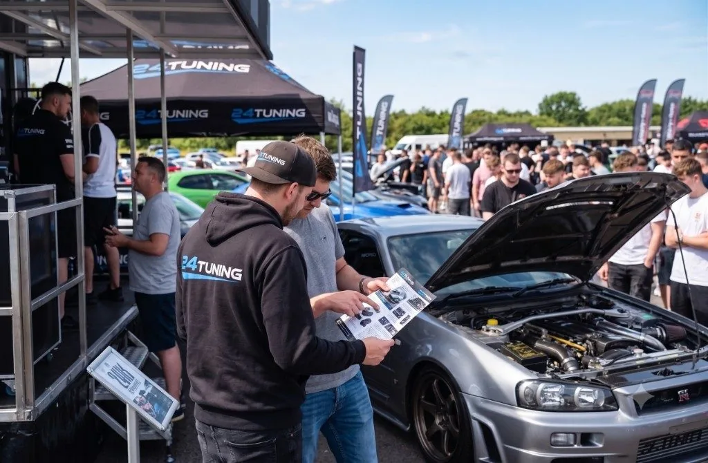 24Tuning team showing a remap brochure beside a silver Nissan Skyline R34 GT-R at the 24Tuning show stand, ECU remapping specialists from Bournemouth, Dorset