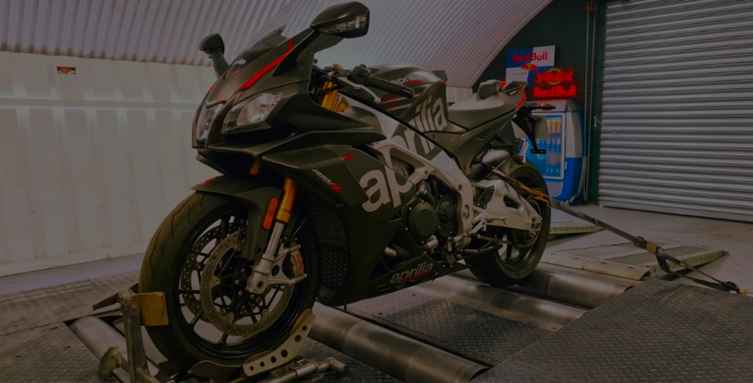 Matte black Aprilia RSV4 1100 front three-quarter on motorcycle rolling road dyno with RSV4 fairing lettering and gold forks at 24Tuning Bournemouth Dorset workshop for Stage 1 ECU remapping