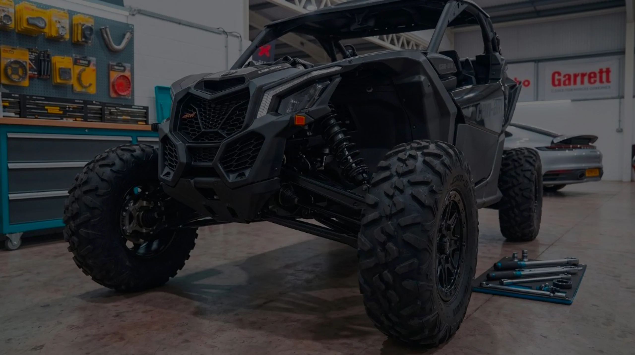 ATV ECU Remap Bournemouth Poole Dorset | 24Tuning Black Can-Am Maverick front three-quarter in 24Tuning Bournemouth Dorset workshop with tool chest, Garrett turbo banner and torque wrenches for ATV ECU remapping