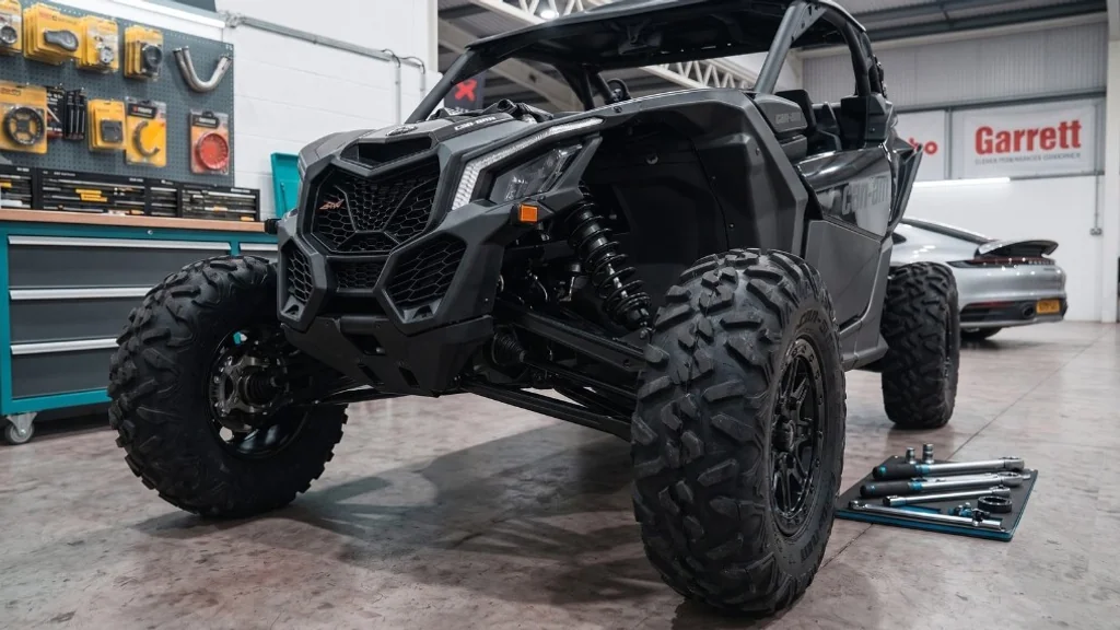 Black Can-Am Maverick front three-quarter in 24Tuning Bournemouth Dorset workshop with tool chest, Garrett turbo banner and torque wrenches for ATV ECU remapping
