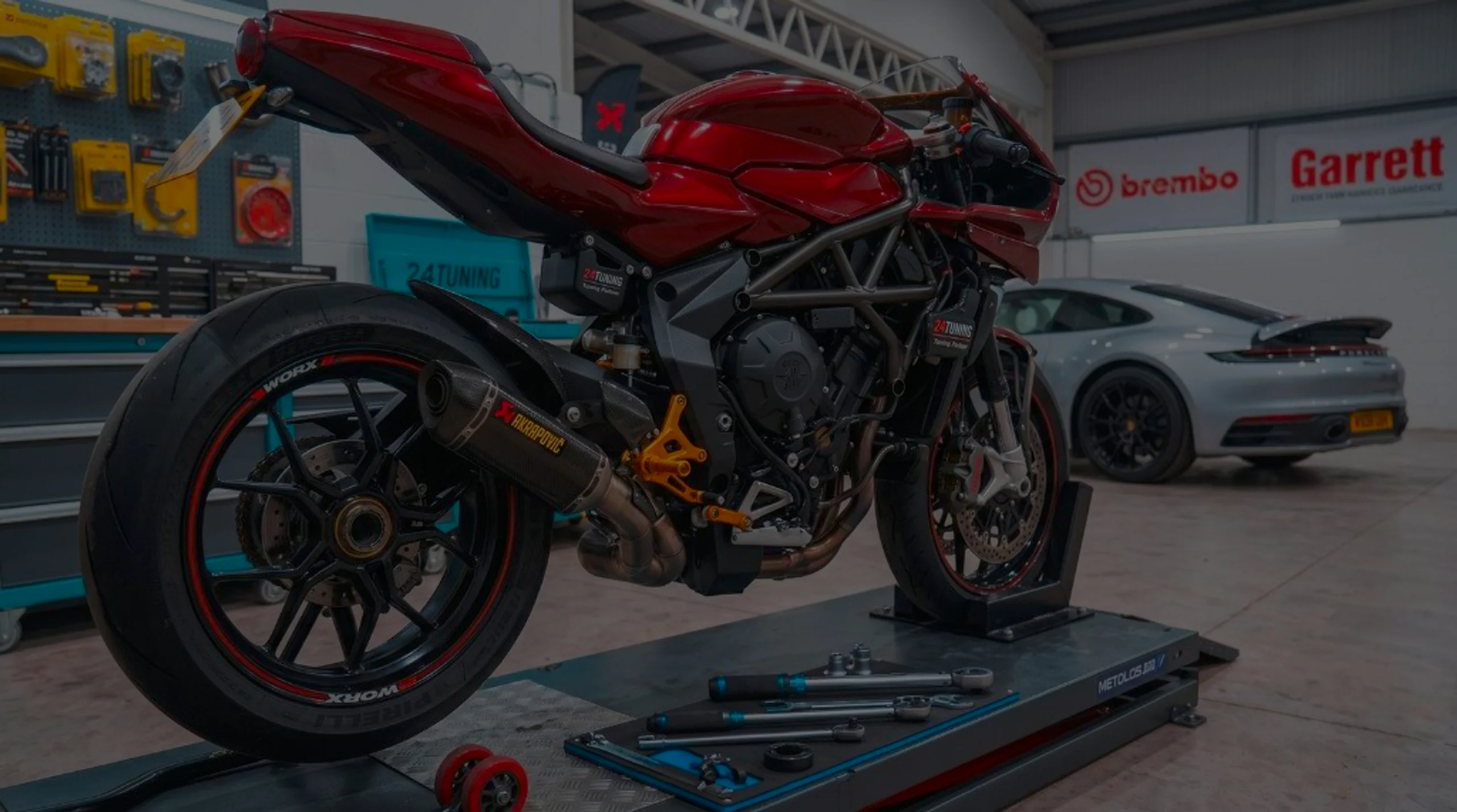 Red MV Agusta Superveloce on motorcycle lift in 24Tuning Bournemouth Dorset workshop with 24Tuning cabinet, Brembo and Garrett tuning banners for motorcycle ECU remapping