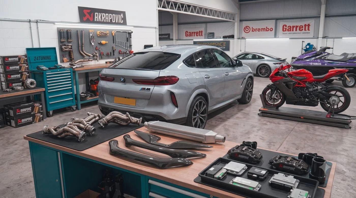 BMW X6 M Stage 1 Remap Workshop Bournemouth Poole Dorset | 24Tuning Silver BMW X6 M in the 24Tuning workshop beside exhaust manifolds, intercooler and ECUs on the bench, ready for a Stage 1 remap, Bournemouth Dorset