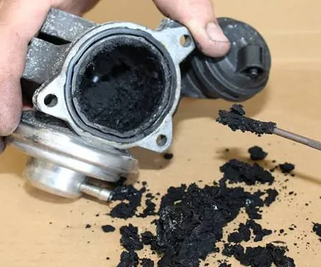 EGR Valve Clean Dorset | 24Tuning Heavily carbon-clogged EGR valve being cleaned, showing soot build-up that causes engine failure