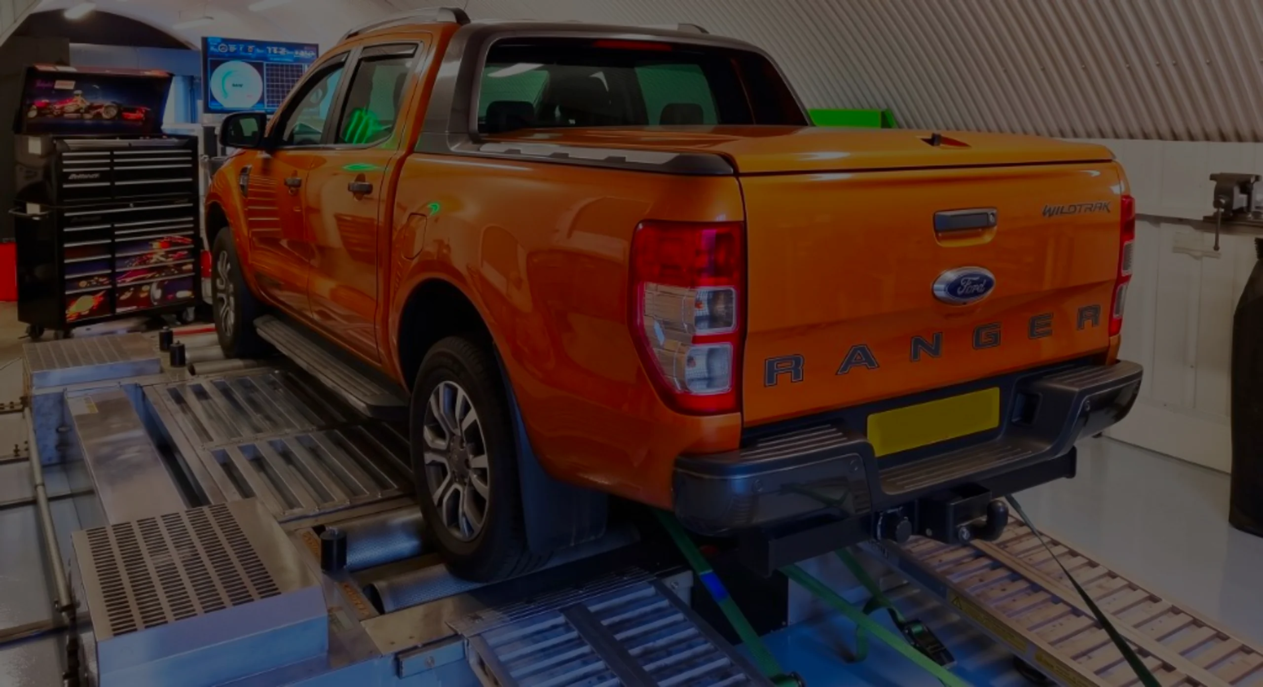 Ford Ranger 3.2 TDCi T6 Remap Bournemouth Poole Dorset | 24Tuning Orange Ford Ranger Wildtrak rear three-quarter on rolling road dyno with RANGER tailgate lettering and green safety straps at 24Tuning Bournemouth Dorset workshop for Stage 1 ECU remapping