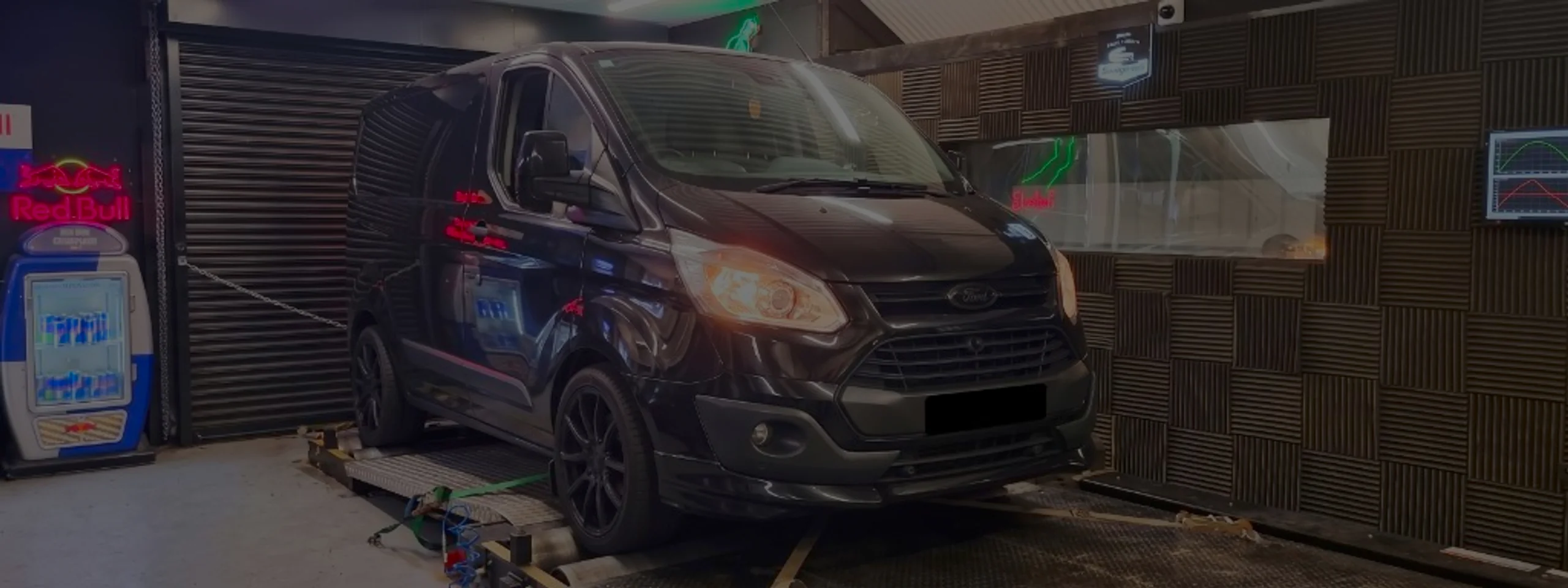 Ford Transit Custom 2.2 TDCi Remap Bournemouth Poole Dorset | 24Tuning Black Ford Transit Custom front three-quarter on rolling road dyno with headlights on and green safety straps at 24Tuning Bournemouth Dorset workshop for Stage 1 ECU remapping