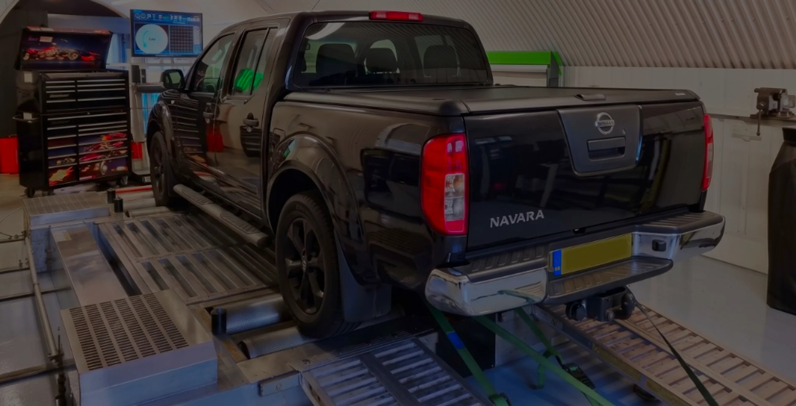 Black Nissan Navara rear three-quarter on rolling road dyno with NAVARA tailgate lettering and green safety straps at 24Tuning Bournemouth Dorset workshop for Stage 1 ECU remapping