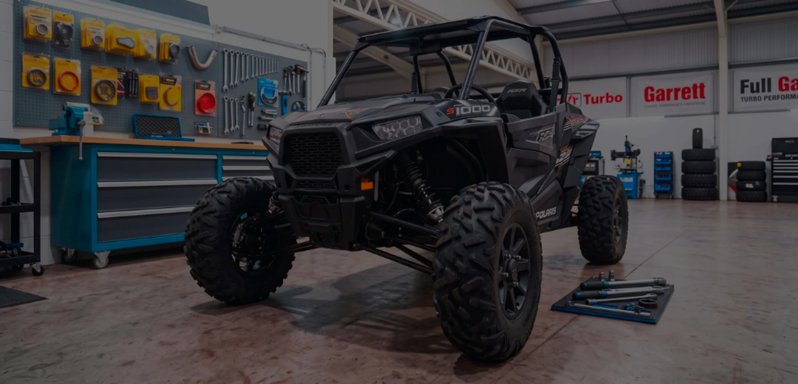 Black Polaris RZR S 1000 front three-quarter in 24Tuning Bournemouth Dorset workshop with S 1000 side decals and Garrett Turbo tuning banners for Stage 1 ECU remapping
