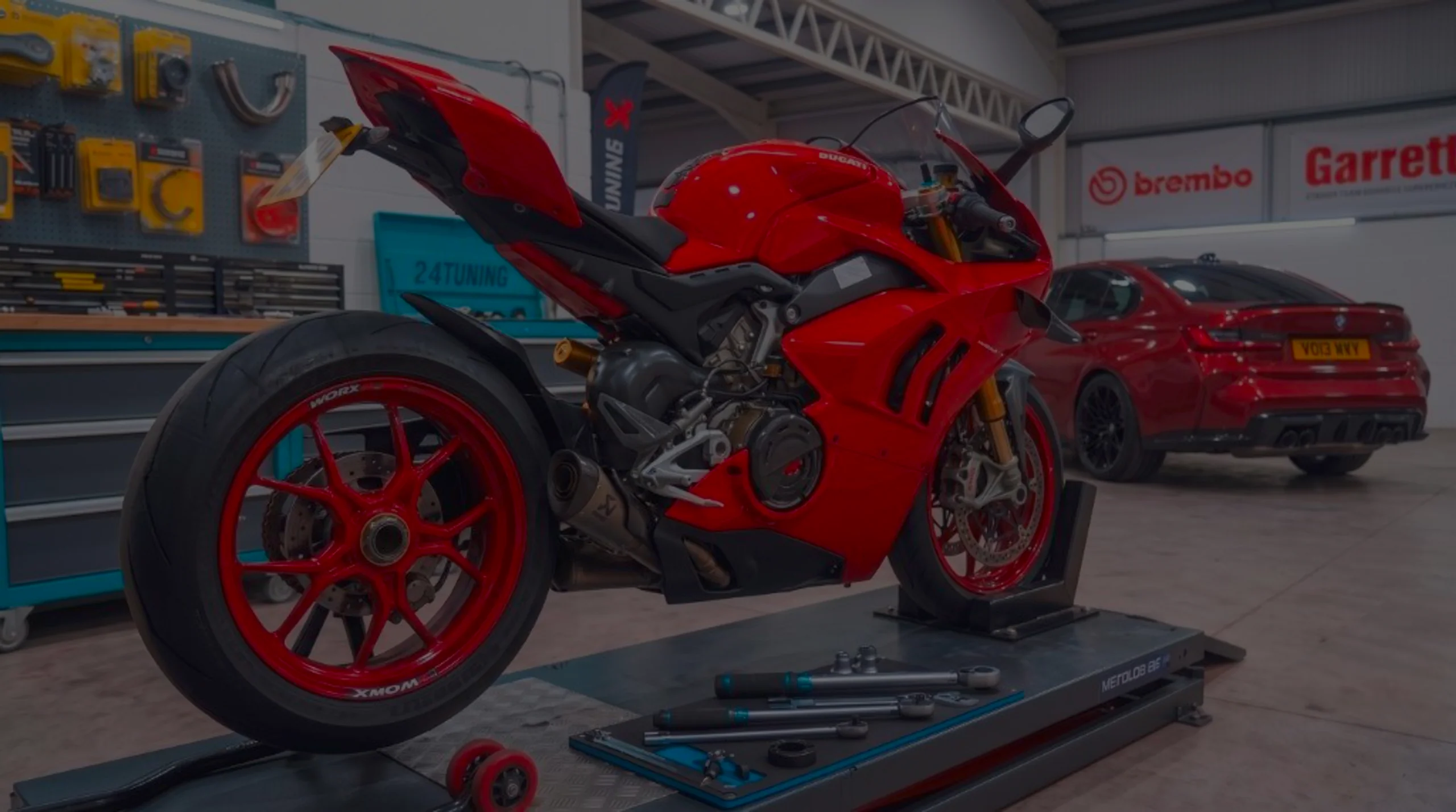 Red Ducati Panigale superbike on motorcycle lift in 24Tuning Bournemouth Dorset workshop with Akrapovic exhaust, 24Tuning cabinet and Brembo tuning banners for superbike ECU tuning