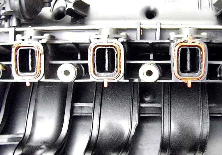 Intake manifold ports with metal swirl flaps and orange gaskets showing carbon buildup — Bournemouth Dorset