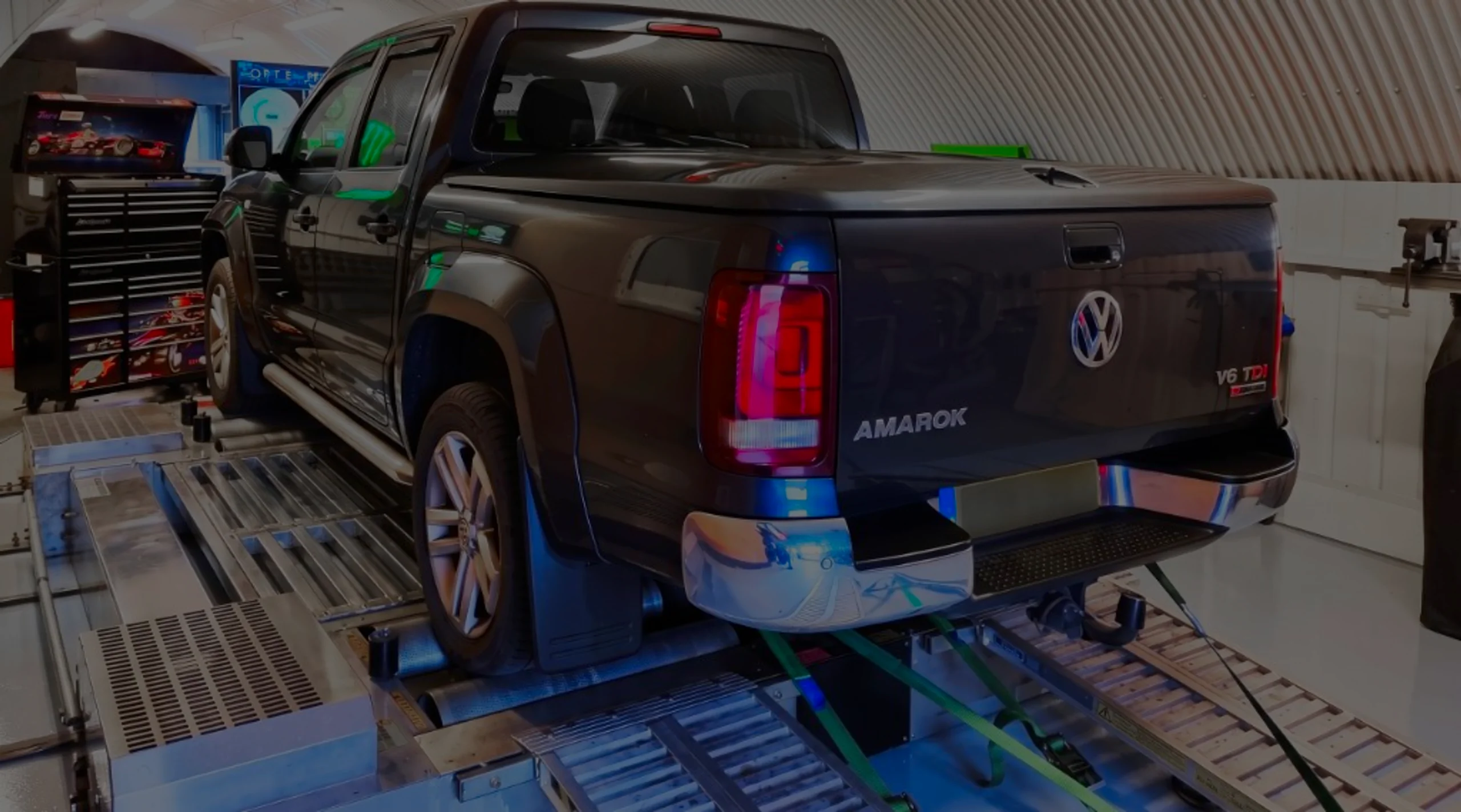 Dark grey Volkswagen Amarok V6 TDI rear three-quarter on rolling road dyno with AMAROK tailgate lettering and green safety straps at 24Tuning Bournemouth Dorset workshop for Stage 1 ECU remapping