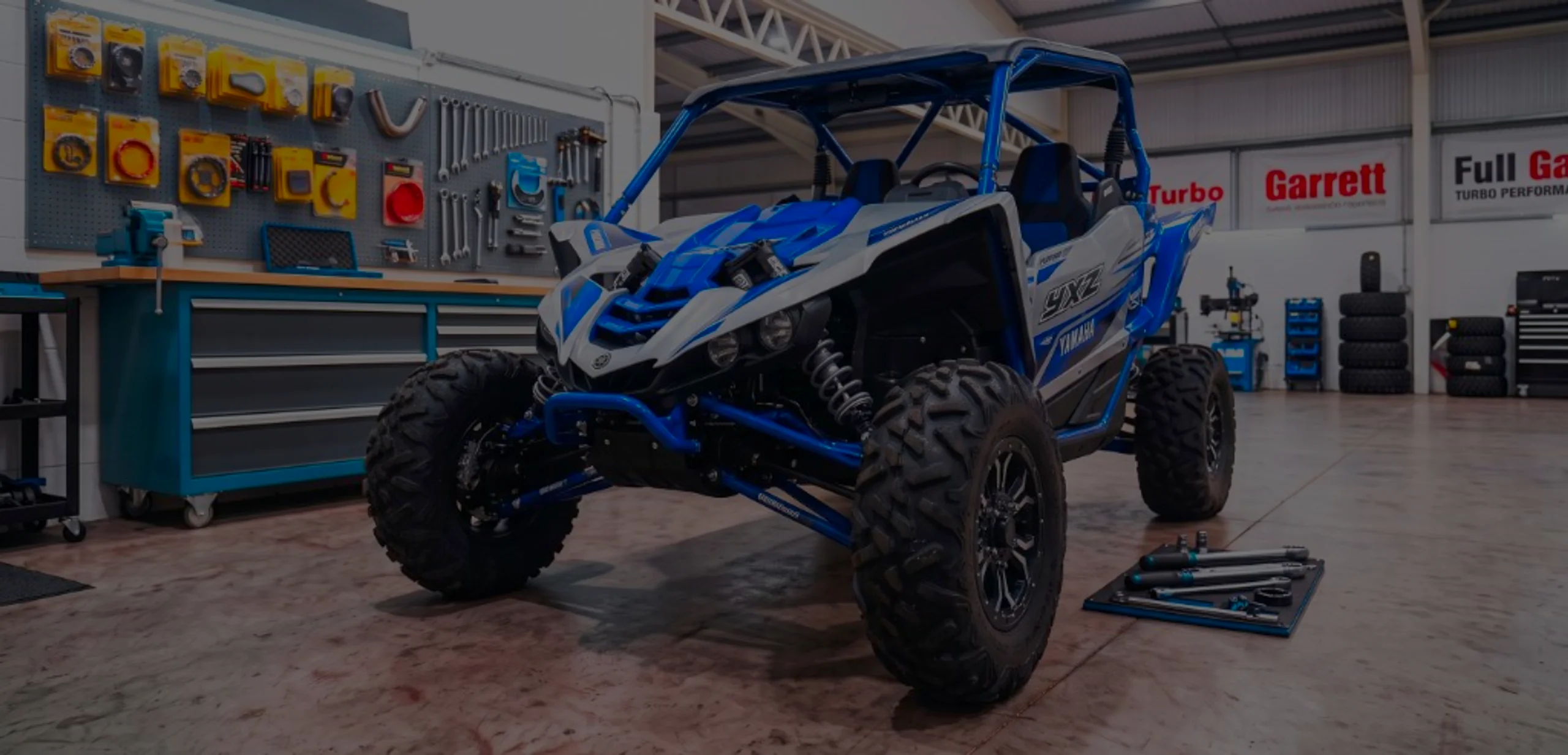 Blue and white Yamaha YXZ 1000R front three-quarter in 24Tuning Bournemouth Dorset workshop with YXZ side decals and Garrett Turbo tuning banners for Stage 1 ECU remapping